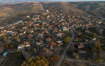 Aerial view of a traditional Turkish village surrounded by hills, showing red-roofed houses, narrow streets, and rural landscape in autumn